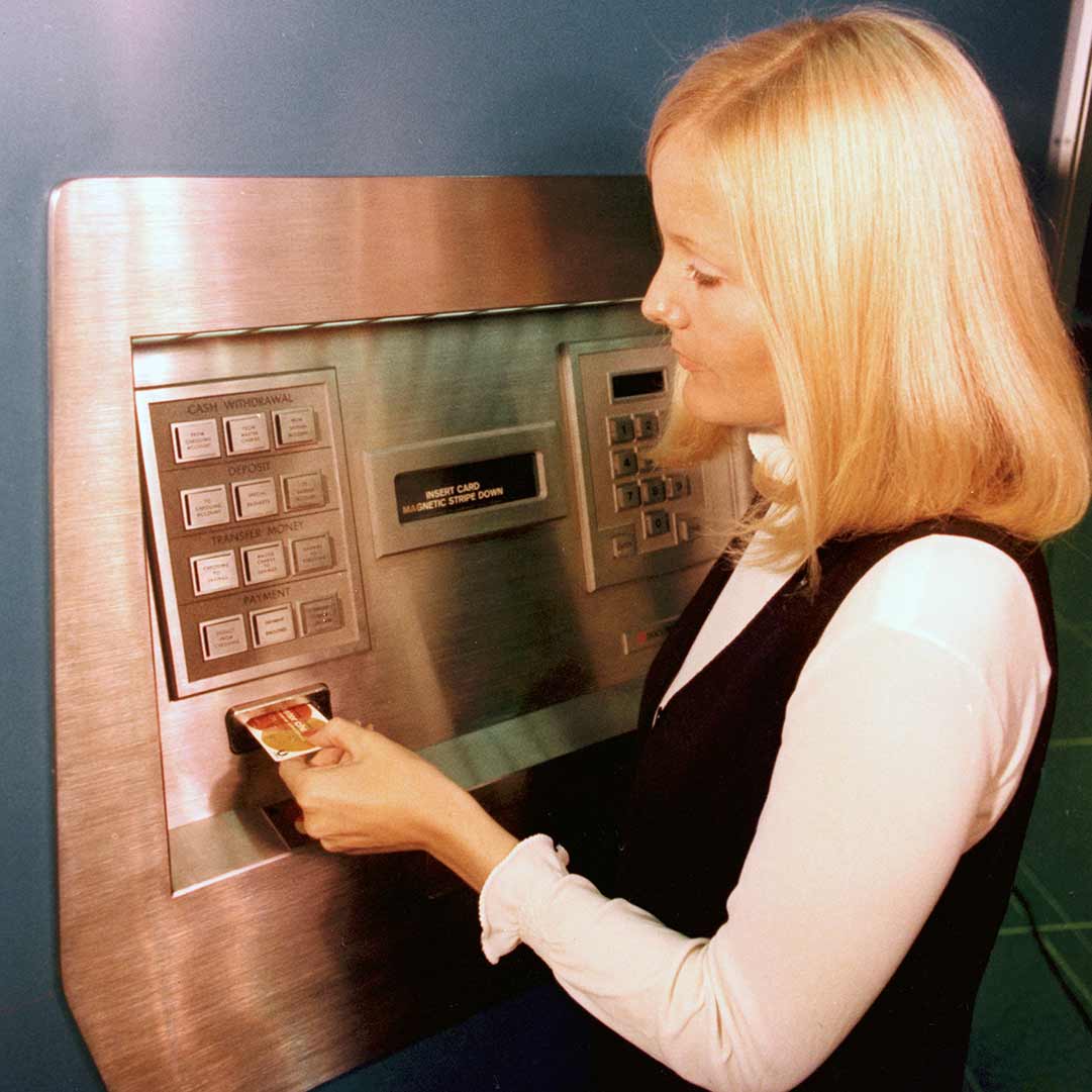 Archival image of a woman withdrawing cash from an old ATM
